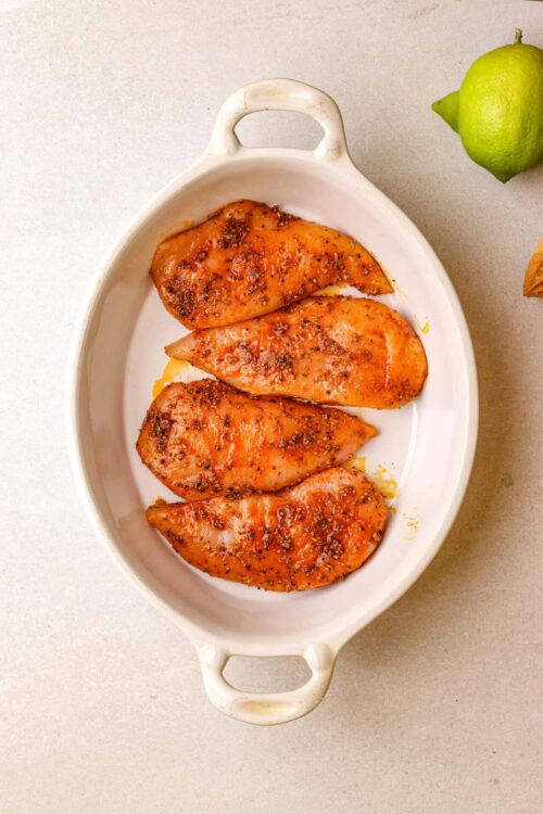 Juicy baked chicken breasts with herbs and spices in a white baking dish.