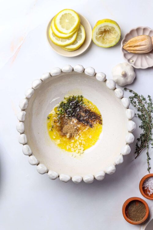 Lemon garlic marinade ingredients in a white bowl with garlic, thyme, and spices around.