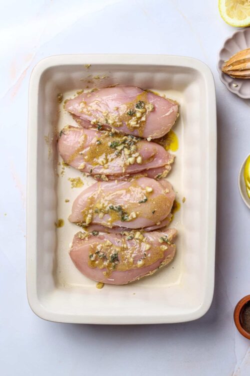 Juicy chicken breasts marinated with garlic, herbs, and lemon in a white baking dish.
