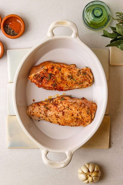 Juicy roasted chicken breasts seasoned with herbs in a white baking dish.