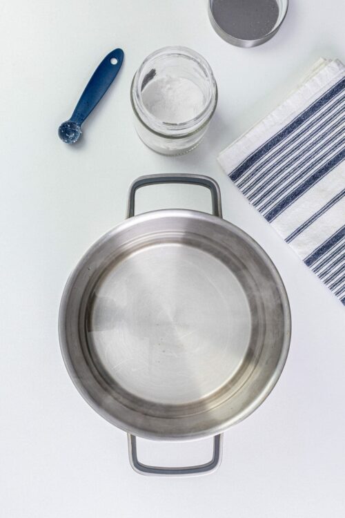 Stainless steel frying pan with kitchen tools and ingredients for baking or cooking.