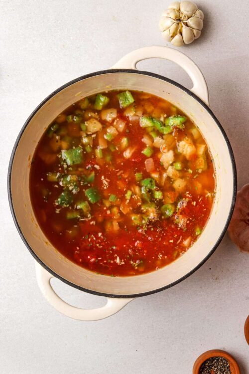 Minced garlic, fresh vegetables, and herbs in a pot of homemade vegetable soup.