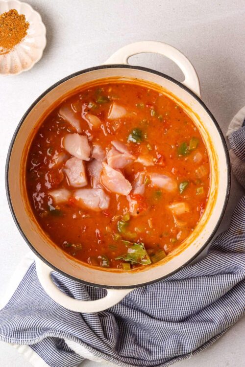 Savory chicken and vegetable tomato soup in a white enamel pot.