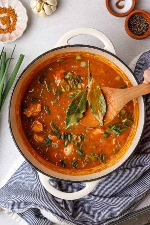 Savory chicken and vegetable hearty soup with fresh herbs in a white ceramic pot.
