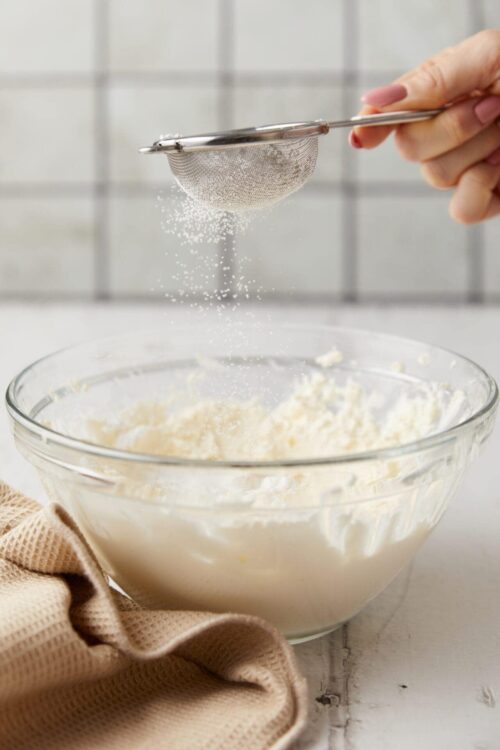 Flour being sifted into a mixing bowl for baking, showcasing baking essentials and process.