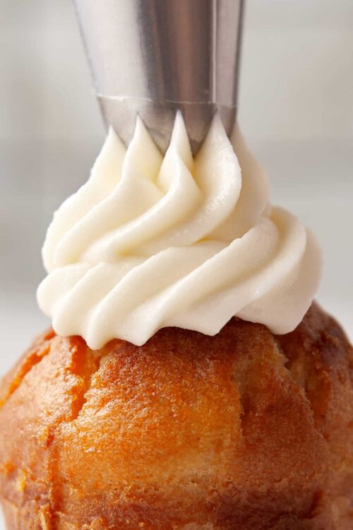 Fluffy vanilla cupcake with swirl of creamy frosting and piping bag tip.