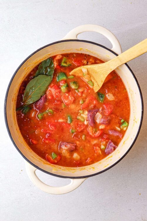 Hearty vegetable soup with tomatoes, beans, and bay leaves in a white enamel pot.