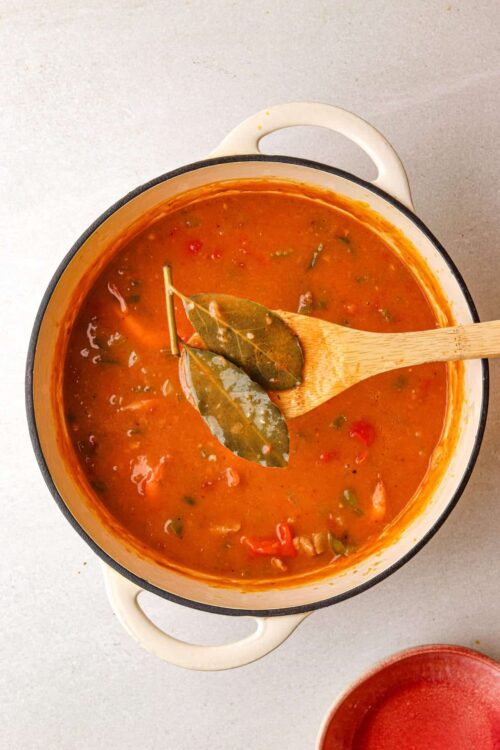 Creamy tomato soup with bay leaves in a white enamel skillet on neutral countertop.