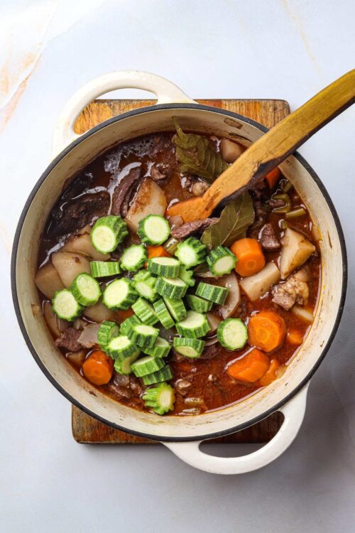 Hearty beef vegetable stew in a white pot with fresh green cucumber garnish on top.