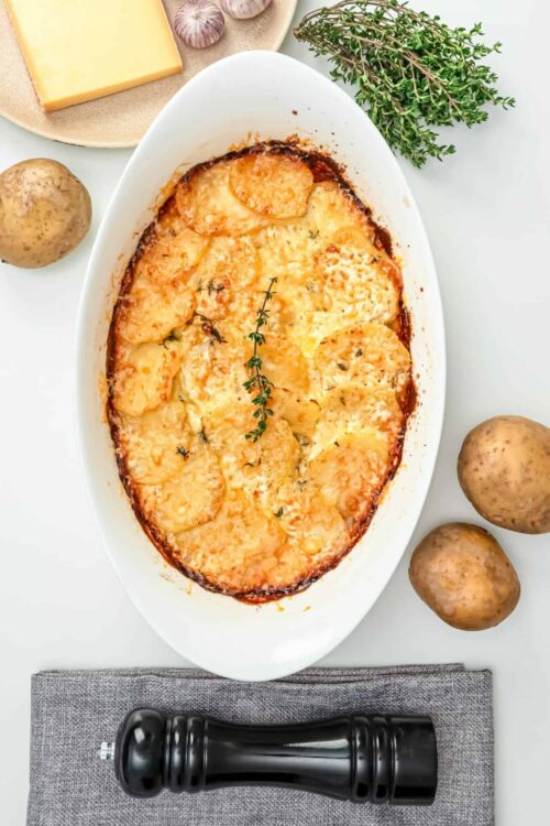 Creamy potato gratin with melted cheese and fresh thyme on a white plate.