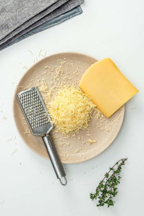 Shredded cheese, a block of cheese, and a cheese grater on a beige plate for baked cheese dishes.