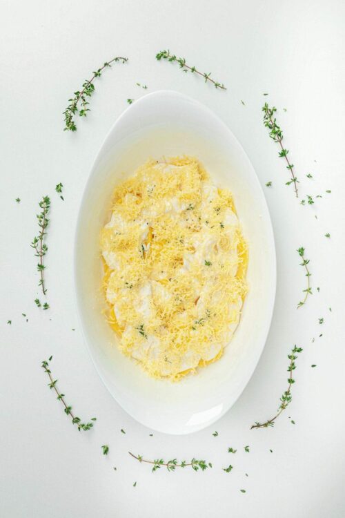 Creamy cheesy mashed potatoes topped with shredded cheese on a white oval platter with fresh thyme sprigs.
