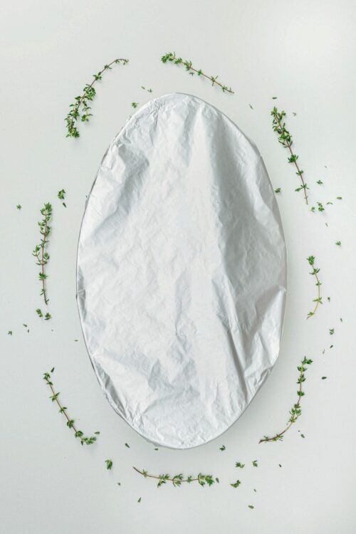 Baked Bree, foil-wrapped dish on a white surface, garnished with fresh thyme sprigs.