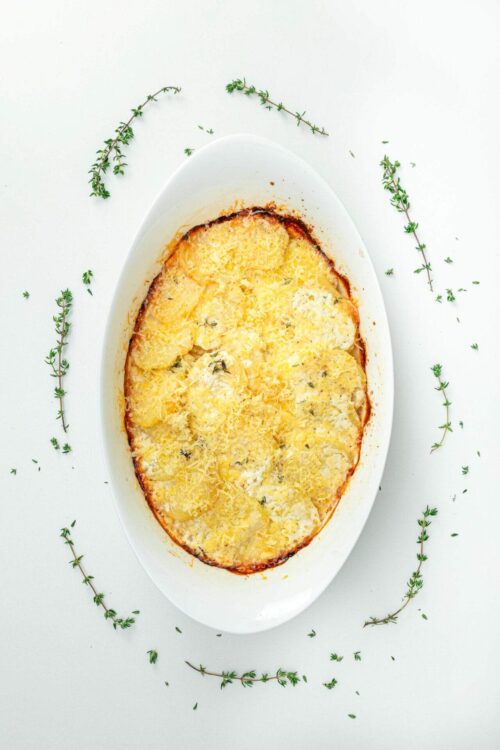 Creamy potato gratin with cheese in an oval baking dish, garnished with fresh thyme.