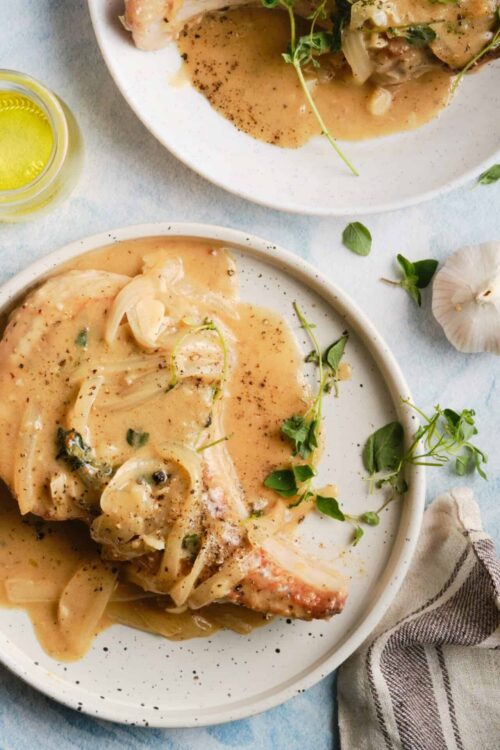 Savory chicken in creamy garlic sauce with herbs on white plates, cheese, and fresh greens.