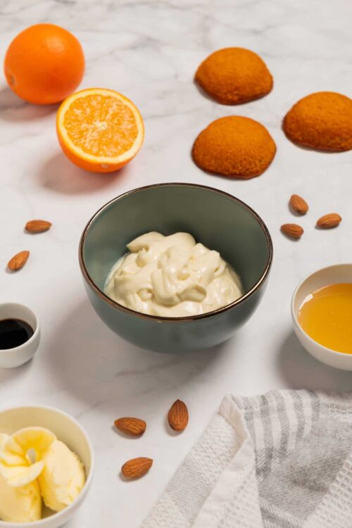 Fresh orange and ingredients for orange flavored baked goods, with a bowl of creamy frosting.