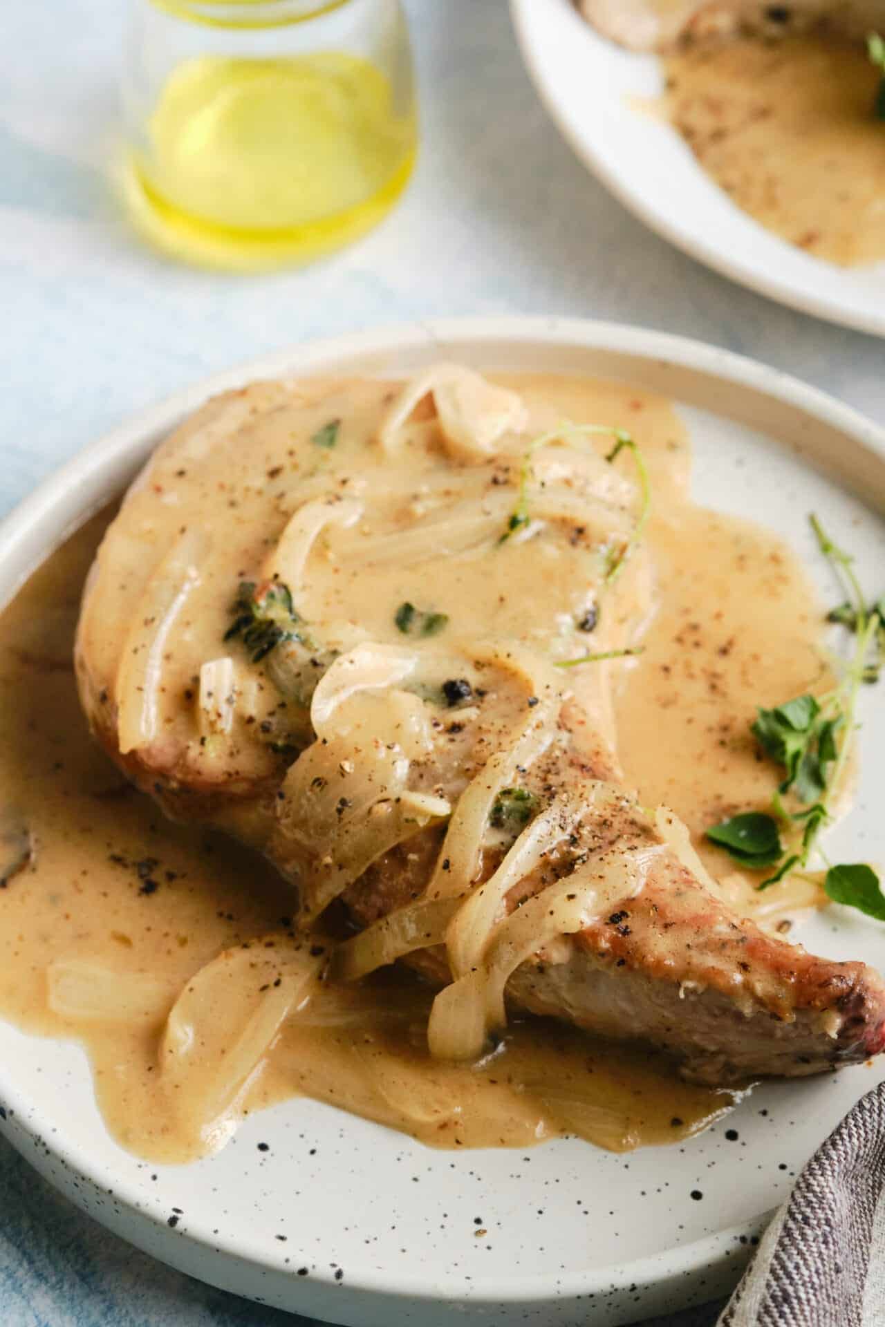 Juicy baked chicken thigh with creamy onion gravy on a white plate.