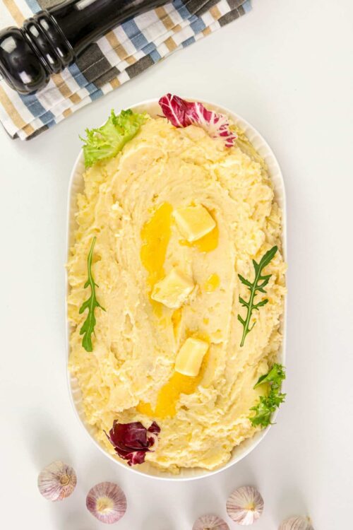 Mashed potatoes with butter and garlic garnished with fresh herbs and leafy greens.