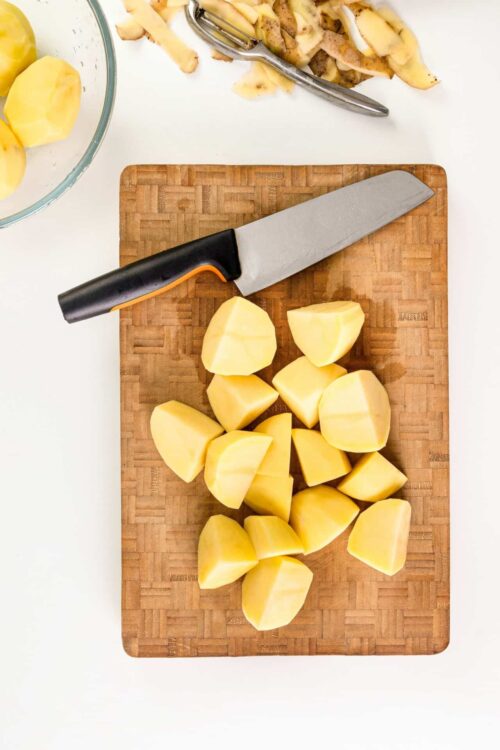 Sliced potatoes on wooden cutting board with chef's knife.