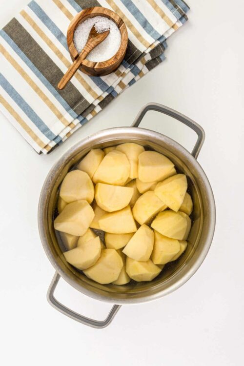 Sweet potatoes boiling in a stainless steel pot on a white surface with a striped dish towel.