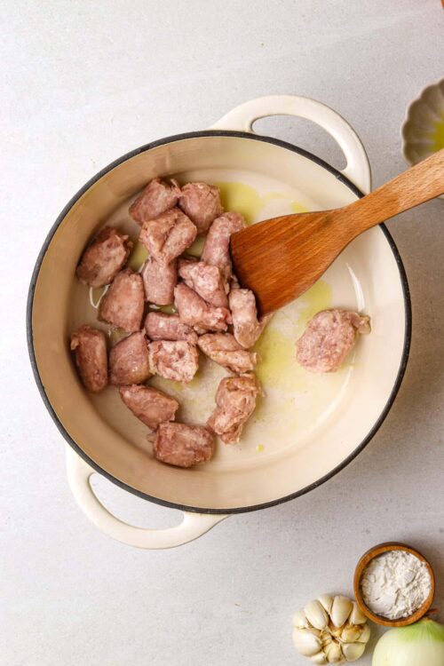 Crockpot sausage ingredients simmering in a white pot with garlic and flour nearby.