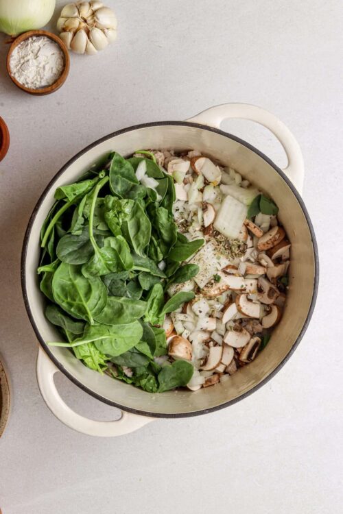 Fresh spinach, chopped onions, and sliced mushrooms in a large pot for cooking, with ingredients for healthy recipes.