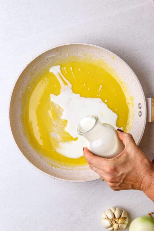 Buttery garlic sauce being prepared in a white skillet with garlic and onion nearby.