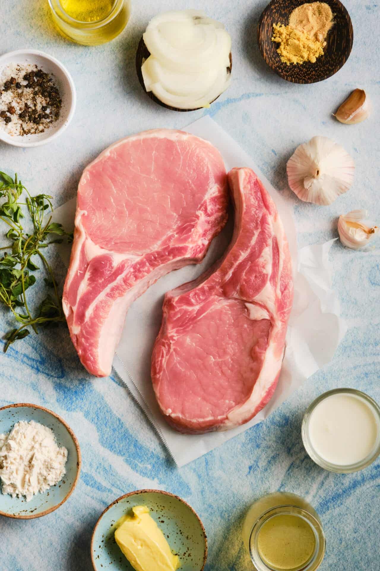 Raw pork chops with herbs and seasonings on a light blue textured surface.
