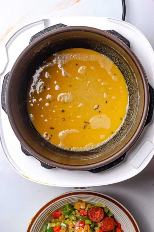 Veloute sauce cooking in a rice cooker with diced vegetables and sausage on a plate.