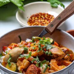 Savory chicken and vegetable stew in a ceramic bowl with fresh herbs and chopped chili flakes in the background.