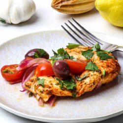 Roasted chicken with cherry tomatoes and herbs on white plate.