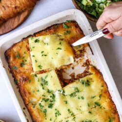 Baked cheesy lasagna in a white baking dish with fresh herbs on top.