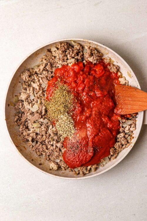 Minced garlic, onion, ground beef, tomato sauce, dried herbs in skillet for cooking.