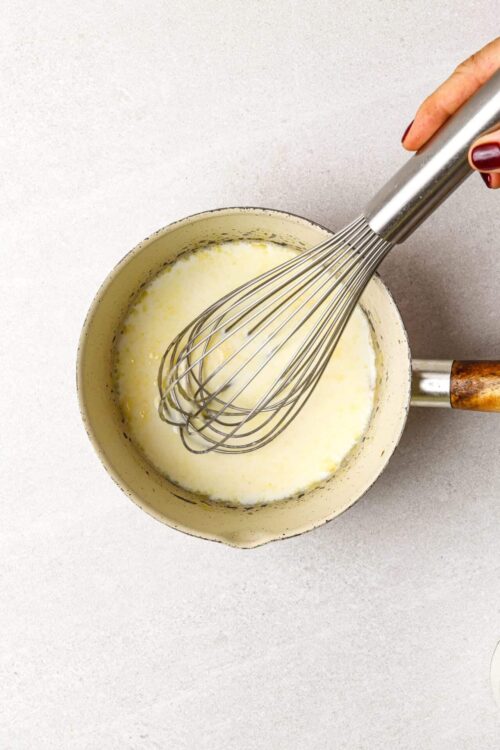 Creamy mixture being whisked in a saucepan with a handheld electric whisk.