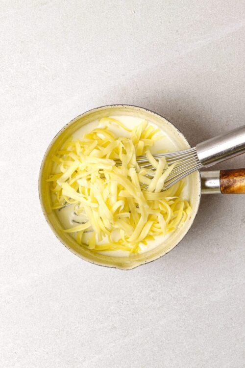 Cream cheese and shredded cheese in a saucepan for cheesy recipes.