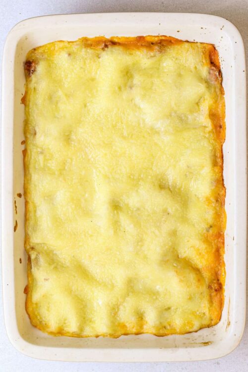 Golden baked cheesy lasagna in a white ceramic dish, rich and delicious homemade comfort food.