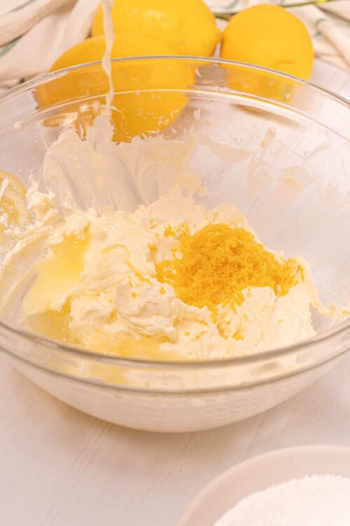Butter, lemon zest, and cream cheese mix in glass bowl for lemon cake batter preparation.