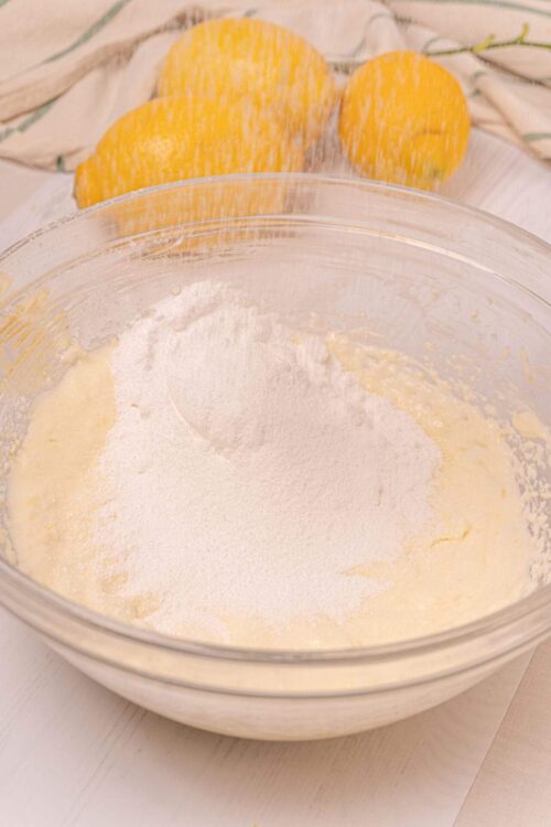Flour in a mixing bowl for baking, with lemons in the background, preparing for a cake or lemon dessert.