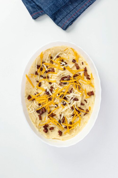 Crispy baked potato with shredded cheese and bacon bits, topped with cheddar and mozzarella, on a white plate.