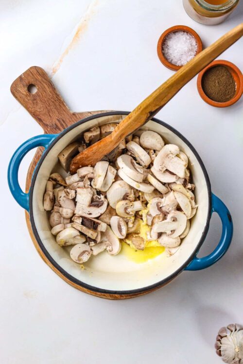 Sautéed mushroom mixture in a white enamel cast iron skillet with wooden spoon.