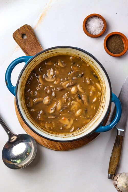Creamy mushroom and herb soup in a blue pot with salt and pepper nearby.