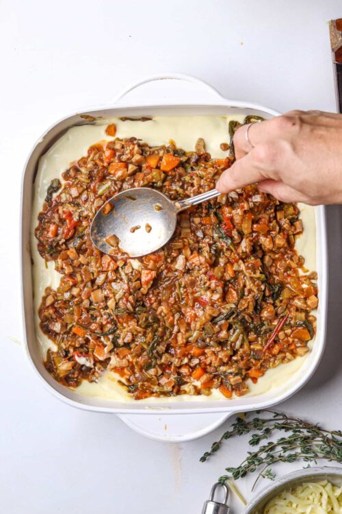 Savory vegetable and mushroom filling layering over creamy mashed potatoes in a baking dish.