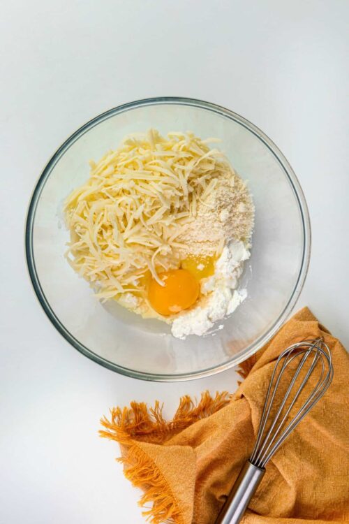 Cream cheese, shredded cheese, eggs, and flour in mixing bowl for baking.