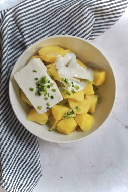 Creamy potato salad with sour cream, chopped green onions, and chunks of yellow potatoes.