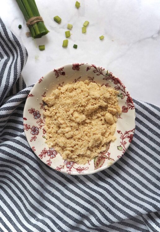 Crumbly pie crust topping in a floral bowl on striped fabric with chopped green onions nearby.