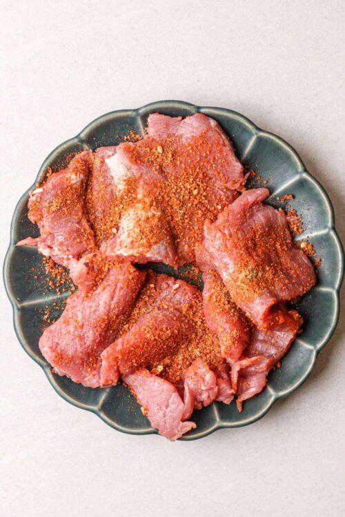 Seasoned raw chicken thighs on a decorative plate for baking or grilling.