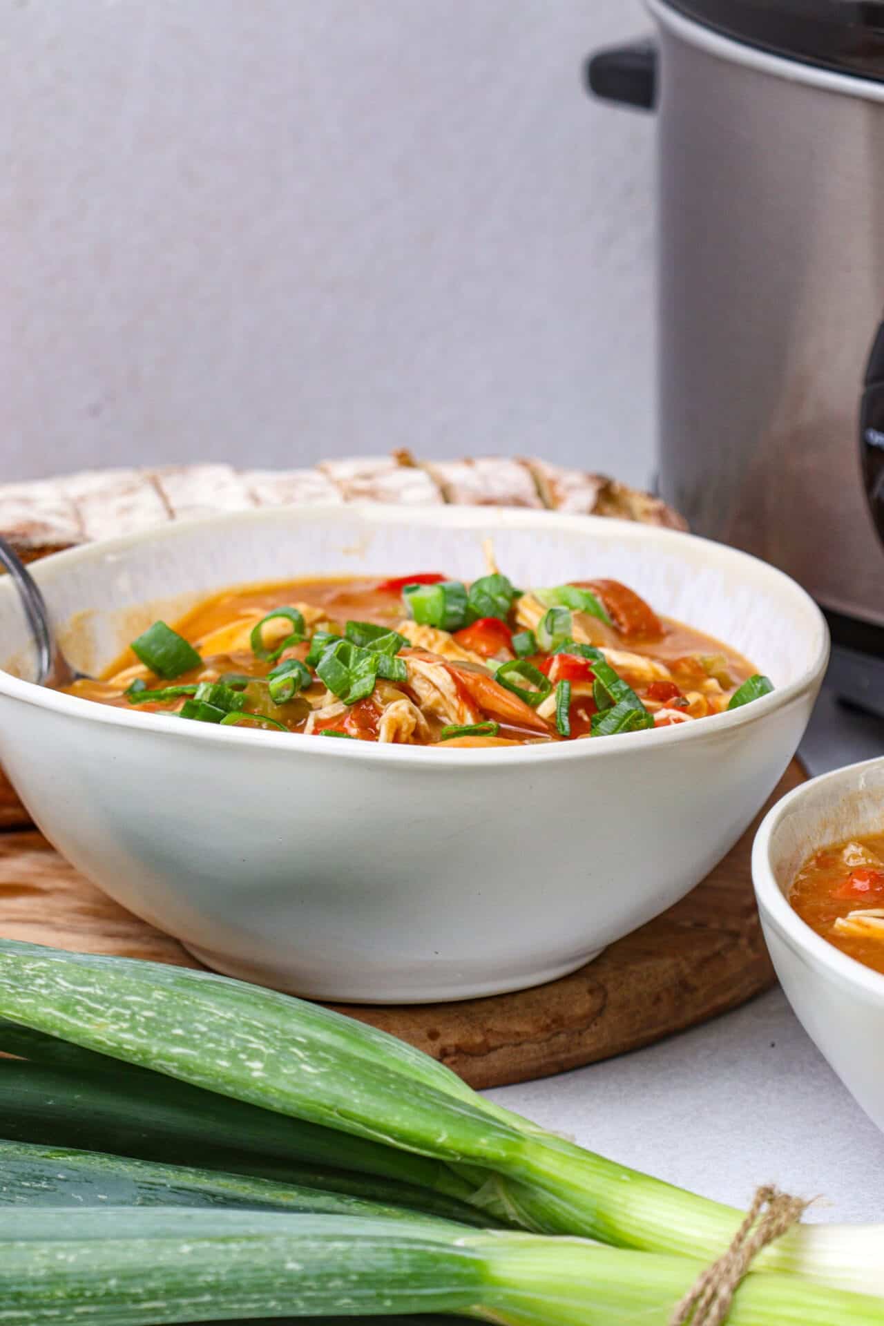 Savory chicken noodle soup garnished with chopped green onions in a white bowl on a wooden board.