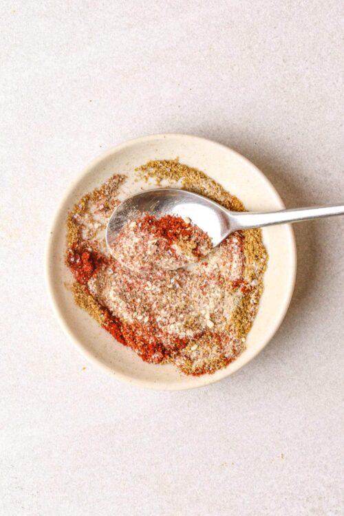 Ground spice blend in a white dish with a silver spoon, used for baking and cooking recipes.