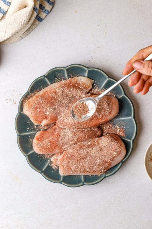 Seasoned raw chicken breasts on blue plate ready for baking or cooking.