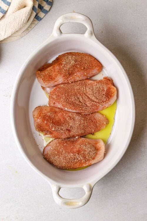 Juicy seasoned chicken breasts in a white baking dish ready to cook.